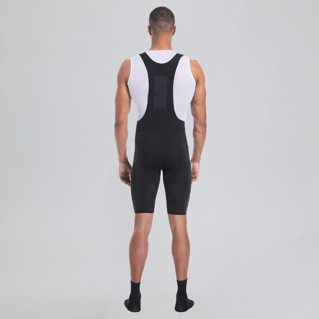 Back view of a model wearing black men's cycling bib shorts over a white sleeveless base layer.
