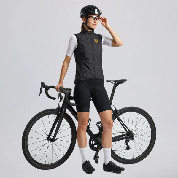 Woman wearing a black windproof cycling vest while standing beside a road bike.