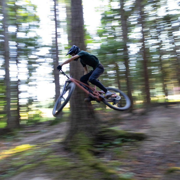 Mountain biker riding through a forest trail, showing Przewalski apparel tested in active outdoor conditions