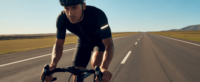 A cyclist dressed in black cycling apparel with reflective elements is riding on the road