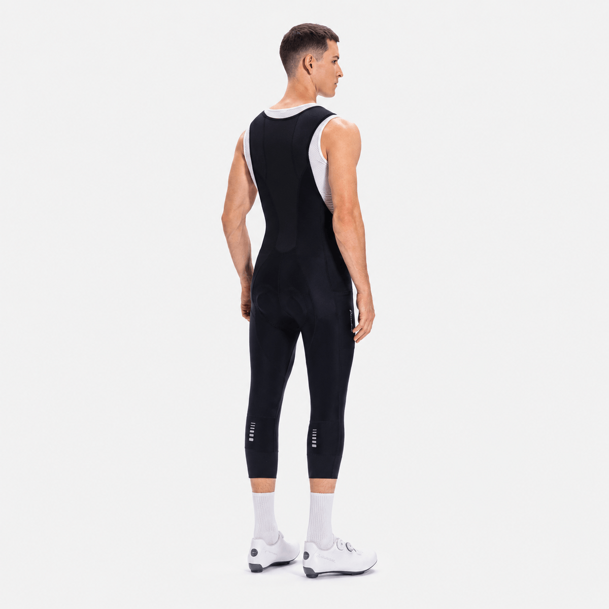 Back three-quarter view of a model wearing black men's classic 3/4 cycling bib shorts.