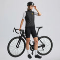Woman wearing a black windproof cycling vest while standing beside a road bike.