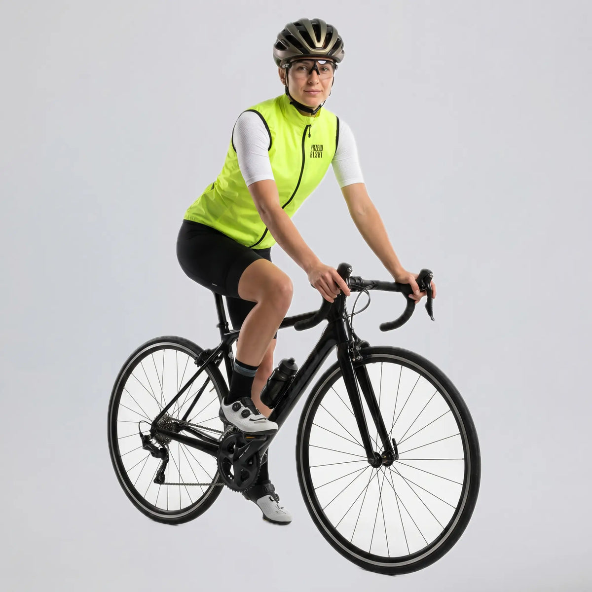 Woman riding a road bike in a bright green windproof cycling vest.