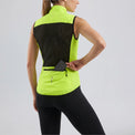 Rear view of a model placing an item in the pocket of a bright green women's windproof cycling vest.