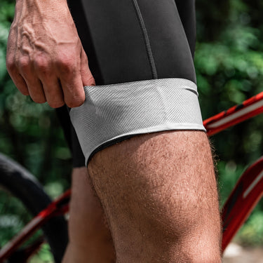 Close-up of a cyclist stretching the leg gripper on black men's cycling bib shorts.